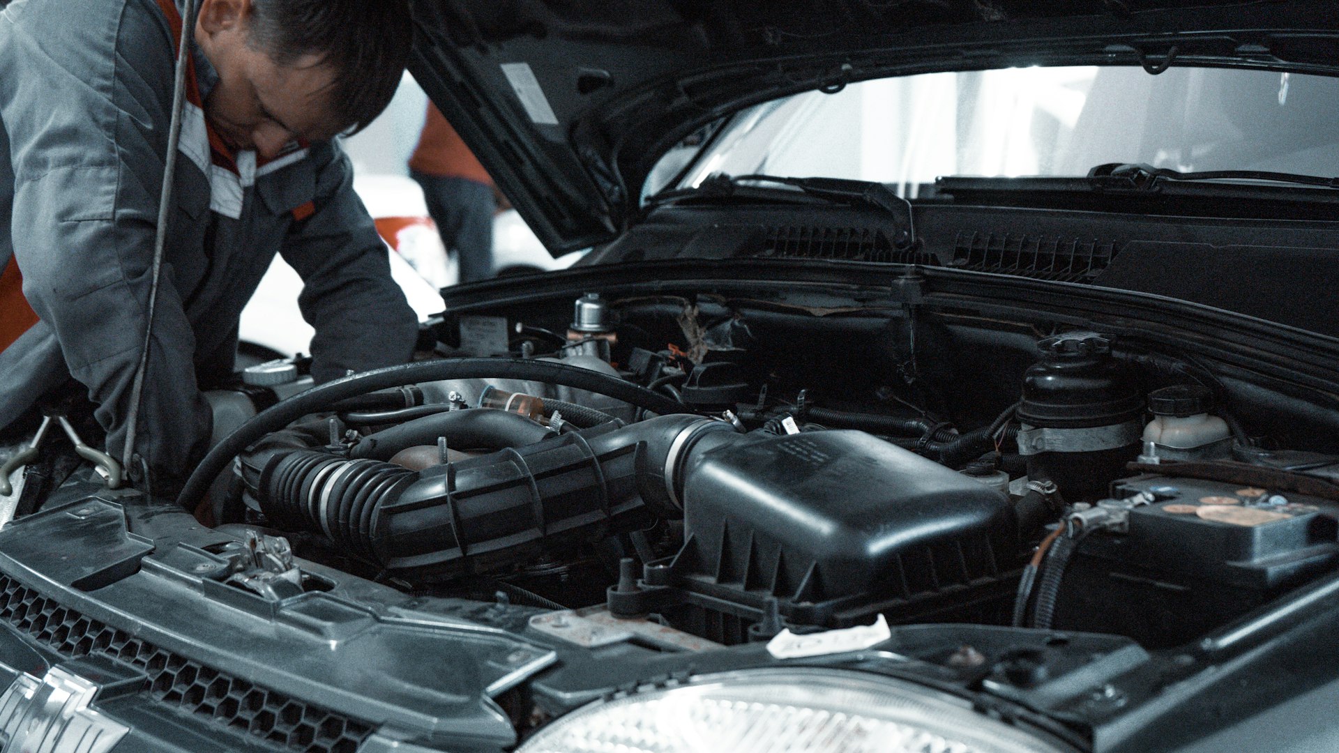 A mechanic checking a car's engine bay and wiring with the bonnet up