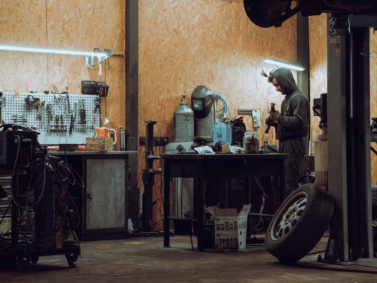 Auto electrician working at the bench under a work light in the Macca's workshop